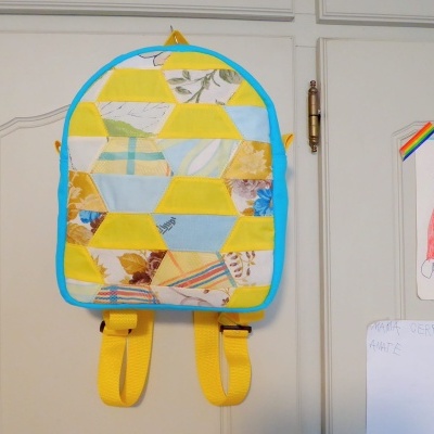 Mochila patchwork colorida pendurada numa porta branca com desenhos de arco-íris ao lado.