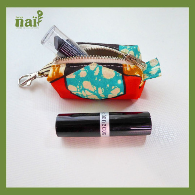 Necessaire colorida com padrão abstrato e batom preto ao lado