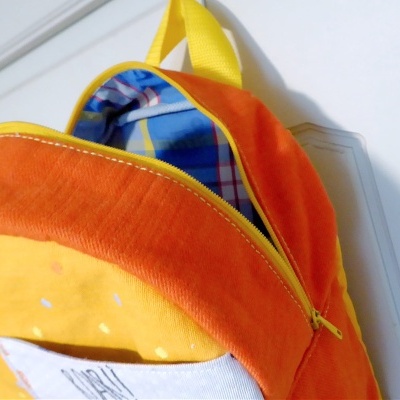 Mochila de pelúcia laranja e amarela com alça amarela pendurada