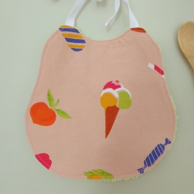 Babete rosa com estampados coloridos e colher de pau ao lado