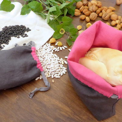 Sacos de pano com feijão e pão sobre mesa de madeira com nozes e folhas