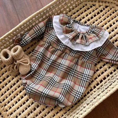 Babygrow xadrez bege com gola branca e sapatos bege numa cesta de vime.