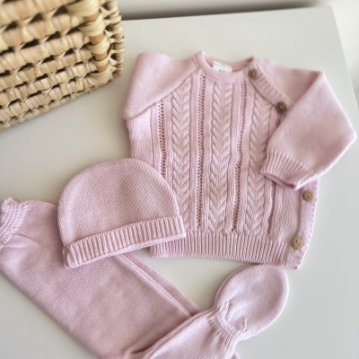Conjunto de roupa bebé rosa em malha com camisola, calças e gorro junto a cesta de verga