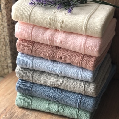 Sete mantas de tricô em cores pastel empilhadas com ramo de flores lilases no topo