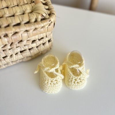 Sapatos de bebé em crochê amarelos ao lado de uma cesta de verga