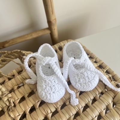 Sapatinhos brancos de bebé em crochet sobre cesto de palha