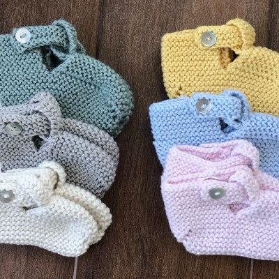 Seis pares de sapatos de bebé em malha colorida com botão sobre madeira.