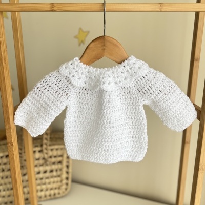 Camisola branca para bebé em croché pendurada num cabide
