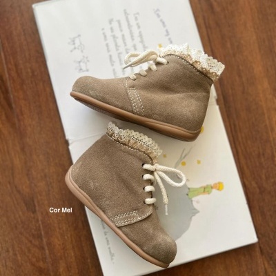 Botas de criança castanhas com renda branca em cima, sobre livro infantil aberto