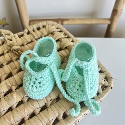 Sapatinhos de bebé verdes em crochet sobre cesto de vime