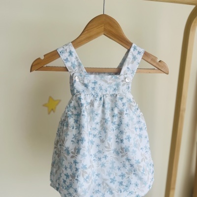 Macacão branco com flores azuis e bege pendurado num cabide de madeira