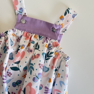 Macacão infantil com padrão floral e alças roxas