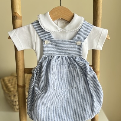 Macacão de bebé branco com jardineira azul às riscas num cabide de madeira