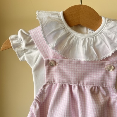Vestido de bebé branco com gola frisada e vestido rosa claro aos quadrados em cabide de madeira