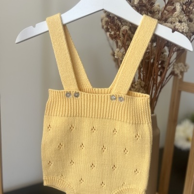Macacão de bebé amarelo em malha com botões, pendurado num cabide branco