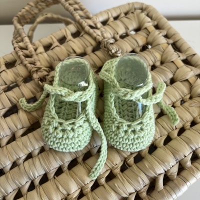 Sapatinhos de bebé verdes em croché sobre mala de palha trançada