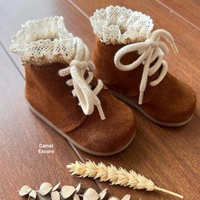 Botins de criança camel escuro com renda branca e atacadores em piso de madeira com ramos secos