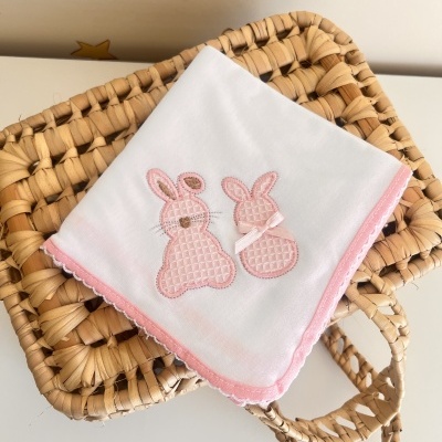 Fralda branca bordada com coelhos rosa sobre cesta de vime trançada