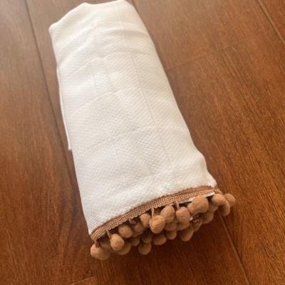 Toalha branca com pompons castanhos numa superfície de madeira.