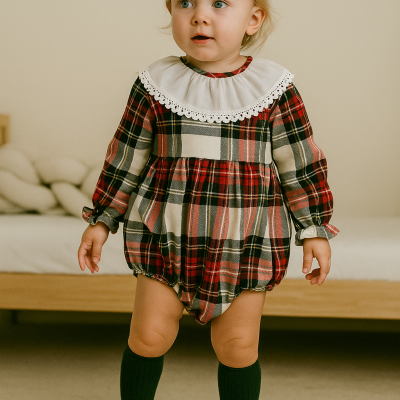 Bebé com roupão xadrez vermelho e gola branca, meias pretas, em ambiente interior.