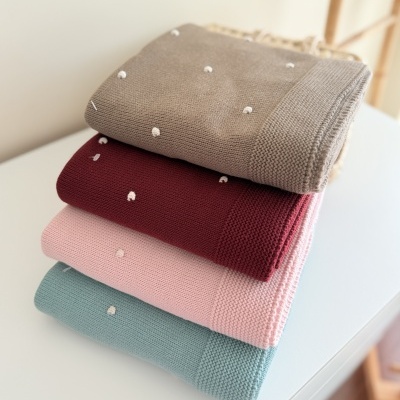 Quatro mantas de tricô em varias cores empilhadas numa mesa branca