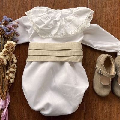 Conjunto de bebé com body branco, cinto bege, sapatos bege e flores secas
