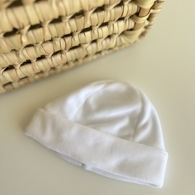 Gorro branco de tecido macio ao lado de cesta trançada