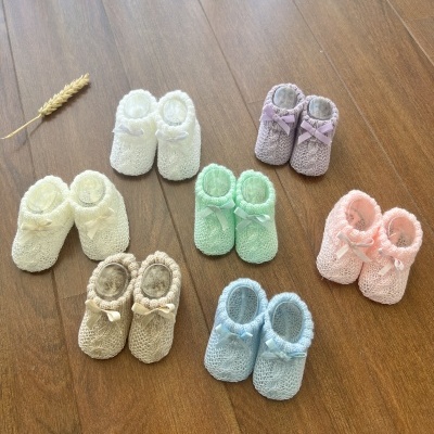 Sete pares de sapatinhos de bebé de tecido coloridos sobre chão de madeira