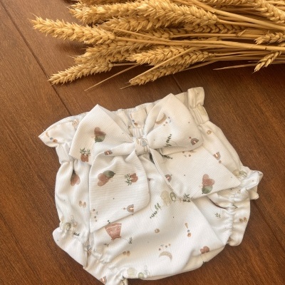 Fralda de tecido branco com laço e padrão de corações e plantas em tons pastel