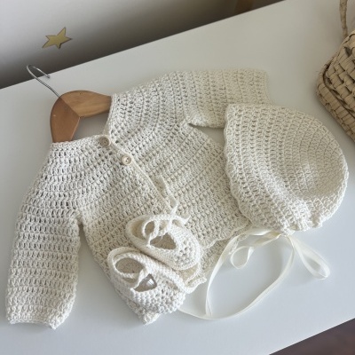 Conjunto de bebé em croché branco com casaco, botinhas e chapéu sobre mesa branca