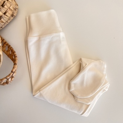 Leggings brancas cremosas em tecido macio sobre mesa branca próximo a cesta de palha