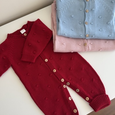 Três macacões de malha para bebé em vermelho, azul claro e rosa claro com botões de madeira.