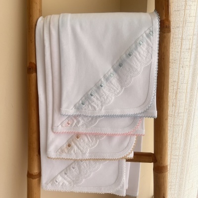 Três mantas brancas com bordados coloridos penduradas numa escada de madeira