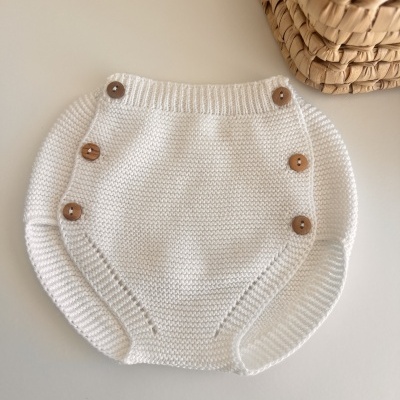 Capa de malha branca com botões de madeira ao lado de cesta de fibra
