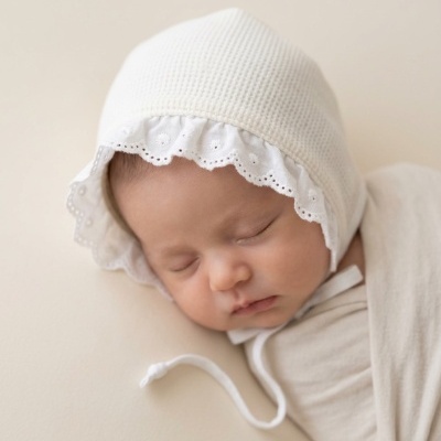 Bebé adormecido com touca branca bordada e manta bege
