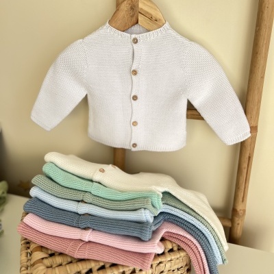 Casaco de malha para bebé em cores pastel com botões de madeira pendurado num cabide de madeira