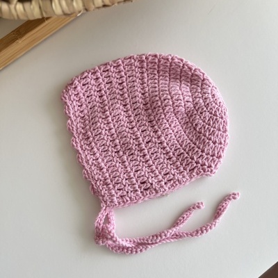 Gorro rosa em crochet com tiras para atar sobre superfície branca