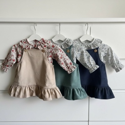 Três vestidos para criança com blusas floridas e saias com folhos em tons neutros pendurados