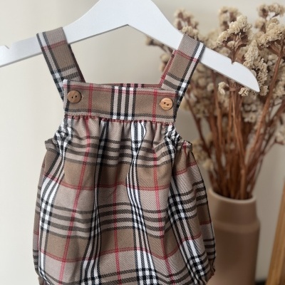 Roupinha infantil xadrez bege com botões pendurada em cabide branco