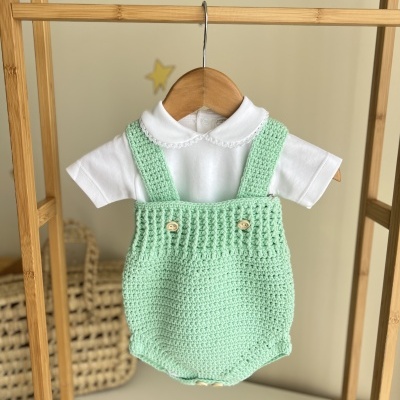 Conjunto de roupa bebé branco e verde água pendurado em cabide dentro de estrutura de madeira