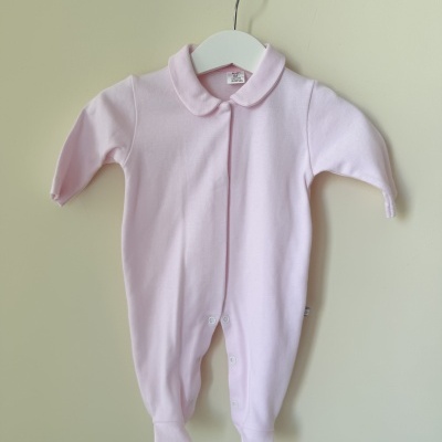 Pijama de bebé rosa claro com gola redonda pendurado num cabide branco
