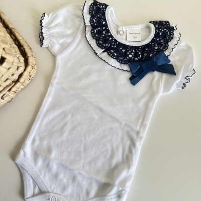 Body de bebê branco com gola rendada azul e laço azul em mesa branca