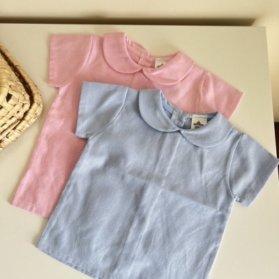 Dois tops infantis de malha em azul claro e rosa com gola tipo Peter Pan, sobre mesa branca