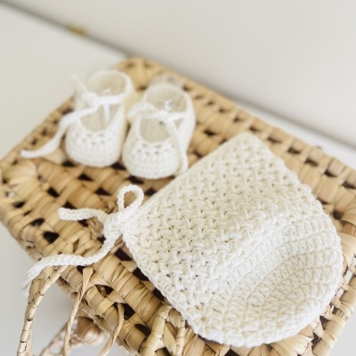 Touca e sapatinhos de bebé em malha branca sobre cesta entrelaçada natural