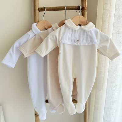 Três macacões de bebé brancos e bege pendurados em cabides de madeira numa estrutura de madeira