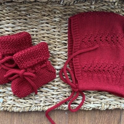 Gorro e luvinhas de bebé em malha vermelha sobre tapete de fibras naturais