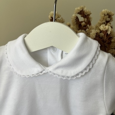 Body branco de bebé com gola redonda bordada pendurado em cabide branco