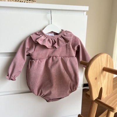 Body de bebé rosa com gola frisada pendurado numa cómoda branca