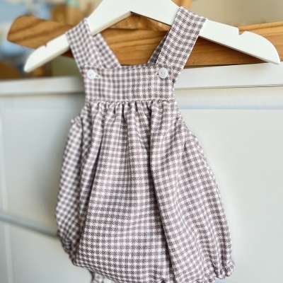 Romper para bebé xadrez castanho e branco pendurado num cabide branco