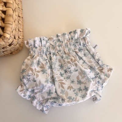 Fralda ou culote floral branco azul e bege para bebé ao lado de cesto de palha